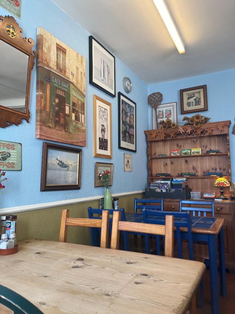 Cosy interior of The Bakery Cafe with traditional wooden tables, blue chairs, and vintage wall art